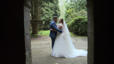 the bride and groom are framed in a stone archway at thornton manor in the wirral