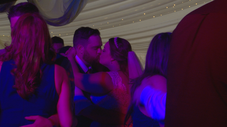 the bride and groom has a kiss on the dancefloor surrounded by their guests dancing at the lakeside marquee