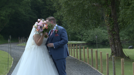 the bride and groom have a sneaky kiss behind her bouquet but the videographer films it