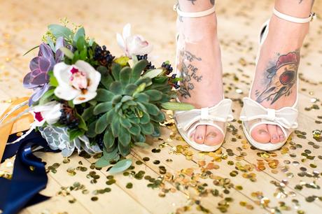 White wedding shoes and bouquet standing on top of confetti on ballroom floor