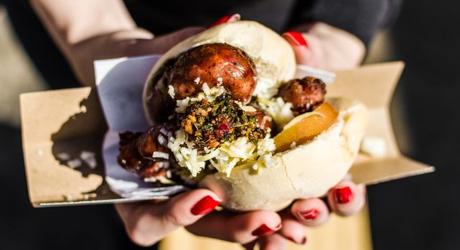 Argentina street food, traditional choripan sandwich with chorizo sausage, tomato, goat cheese, and chimichurri sauce at a street food market