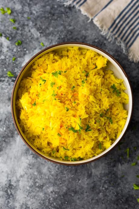 saffron rice in brown bowl with green herbs sprinkled on top