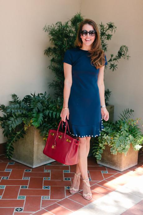 Amy havins wears a navy shift dress with pearl details.
