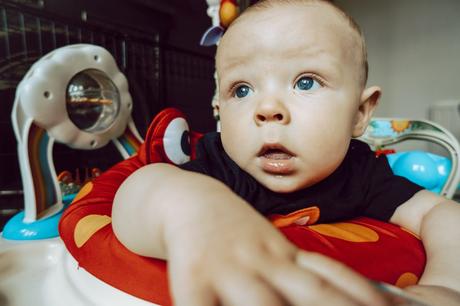 a close up photo of a blue eyed boy pausing from the bouncing in his jungle themed jumperoo in the living room of his house in Sale