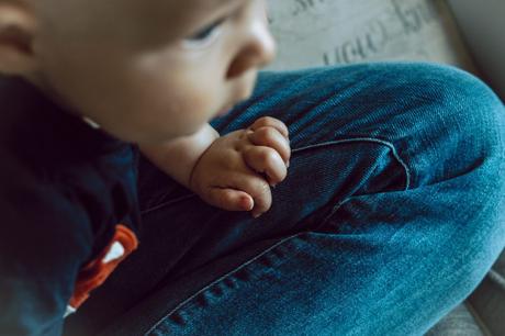 a close up of a little boys hand leaning on his Daddy's knee as they watch tv together at home in Manchester