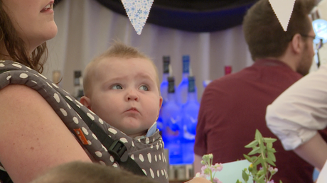 a cute baby girl looks up confused in a carrier on her mum at Alder Root Golf Club marquee for a christening party