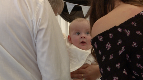 a baby looks wide eyed at a guest pulling faces at them at a christeing party at Alder Root Golf Club in Warrington