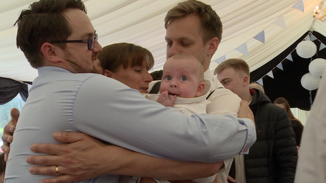 a big family hug with a baby boy Archie in the middle looking confused  at a christeing party at Alder Root Golf Club in Warrington