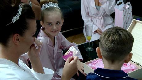 a flower girl looks on as the bride tries to hold the tears back on the wedding video after opening her future husbands wedding gift