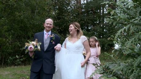 a groom smiles at the videographer as the bride laughs and holds his hand walking down the hill at Abel's Harp