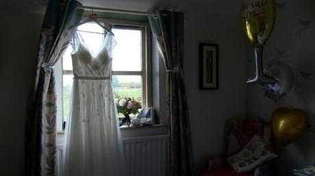 a vintage inspired wedding dress hangs on a wooden bridal hanger in front of a bright window at Abels Harp in Shrewsbury