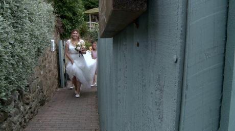a bride walks beside a pretty green fence as her daughters carry her train at abels harp