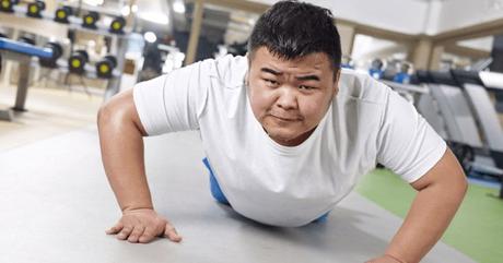 An obese man attempting a push-up in a gym.