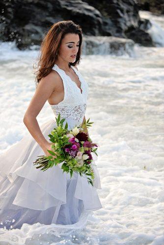 beach styled shoot bride in a white dress with bouquet elegant makeup is standing in the sea alexi