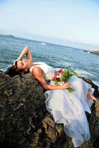 beach styled shoot bride with a bouquet lies on the rocks against the sea alexi