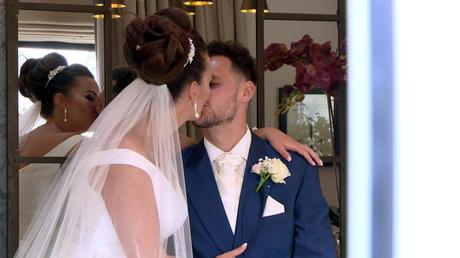 a bride and groom enjoy a relxed kiss between photos as the videographer catches a more natural moment from behind a door at Thornton hall