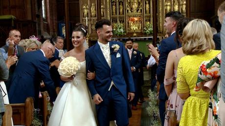 the bride and groom walk back up the aisle at St Savious church in wirral and the bride holds a classic ivory rose bouquet