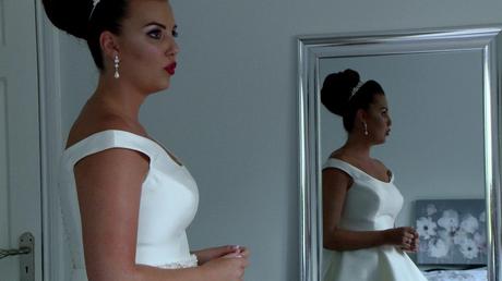 a classic old hollywood style bride takes a deep breath pouting her red lips with her reflection in the mirror behind her on the wedding video