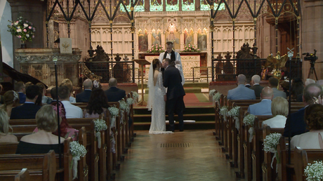 The bride and groom kiss as the priest announces you may kiss the bride in front of family, friends and the wedding videographer at St Peter's Church in Woolton Liverpool