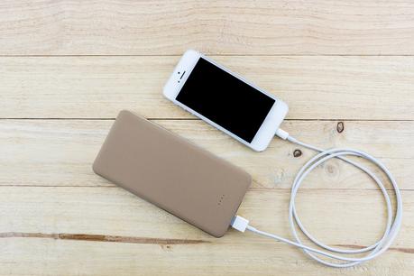 Smartphone with golden powerbank on wood desk.