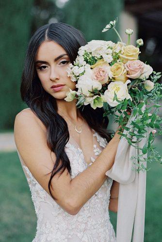 besame wedding styled shoot bride with dark loose hair holding a cascading bouquet with peach black pink roses and greenery carrie king photographer