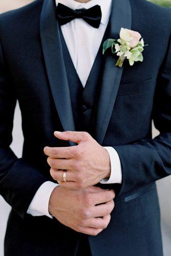 besame wedding styled shoot groom with a butterfly in a black suit with a waistcoat and a buttonhole of roses on his finger a simple gold ring carrie king photographer