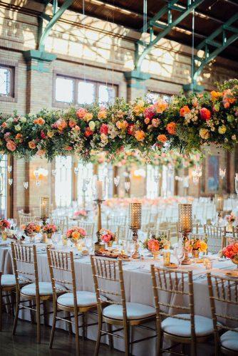 wedding decor 2019 orange and coral flowers and greenery hanging above table with tall candle centerpieces tim tab studios