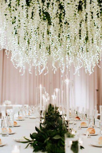 wedding decor 2019 hanging floral installations white flowers and lighting garland above table with candles and greenery tablerunner haley ringo photography