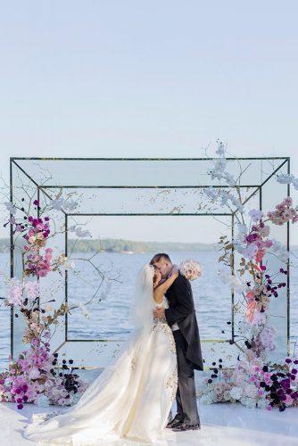 wedding colors 2019 groom and bride kissing geometric backdrop decorated with violet crocus and pink flowers roman_ivanov_weddings