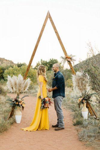 mustard wedding bohemian groom and bride under triangle wooden arch with flowers and pampas grass levi tijerina