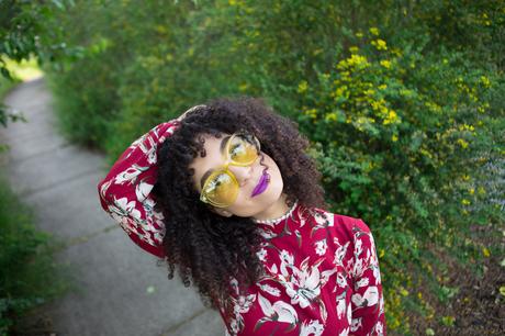 Amber wearing a red floral dress, wearing purple lipstick and yellow sunglasses