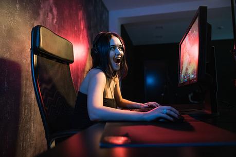 A cute female gamer girl sits in a cozy room behind a computer and plays games. Woman live streaming computer video games to her fans and wiggle hand to them. Streamer and gamer concept