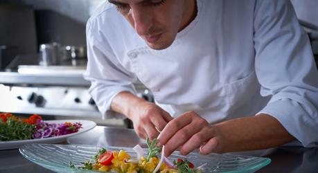 Chef garnishing ceviche dish with hands in stainless steel kitchen