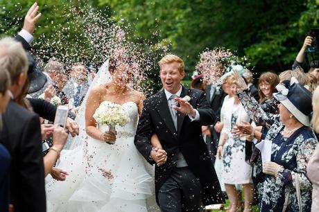 bride and groom walk through a storm of confetti at hengrave hall