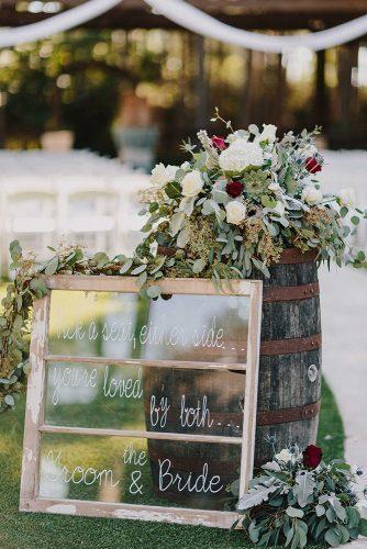 bohemian wedding decorations signs on old window frame near with wine barrel and red flowers kristen curette photography