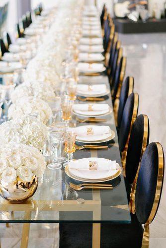modern wedding decor ideas reception glass table with white flowers in gold vases and black velvet chairs lindseyboice