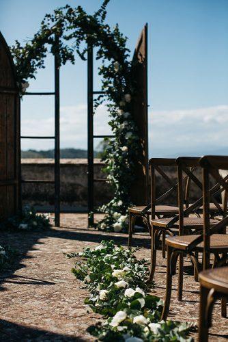summer wedding trends outdoor ceremony with wooden door altar and greenery aisle with white roses stefano santucci studio