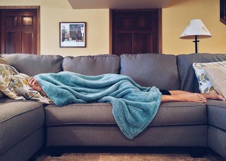 A person lying on a sofa under a blanket