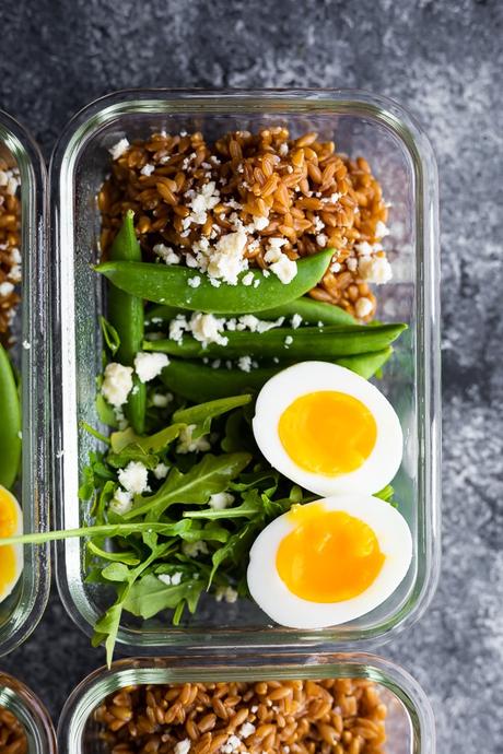 overhead view of arugula salad with farro and eggs in meal prep container