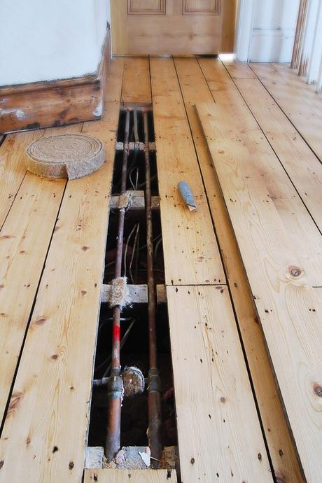 a floorboard that has been taken up to reveal pipework under the floor