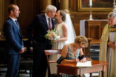 bride and groom kiss as a witness signs