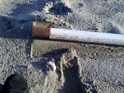 Image of rusty pole in the sand and foot print