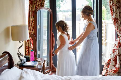 the brides sister helps her into her dress