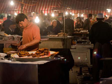 Uighur man slicing fried fish at the night market