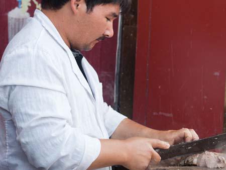 Uighur man slicing goat meat