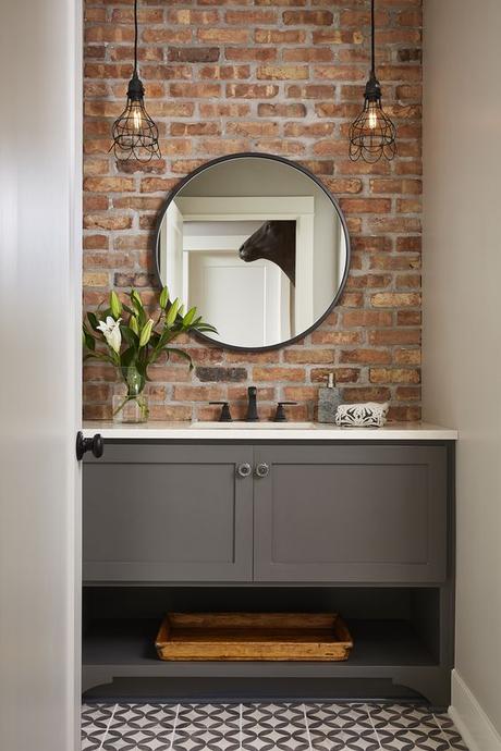 basic gray single sink bathroom vanity with brick accent wall and circle bathroom mirror