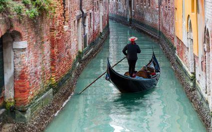 Enchanting Travels Italy Tours Venetian gondolier punting gondola through green canal waters of Venice Italy