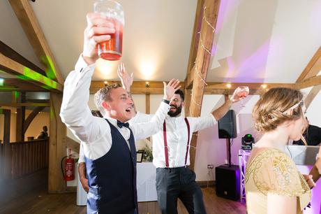 Guests dance holding their beer at wedding. 