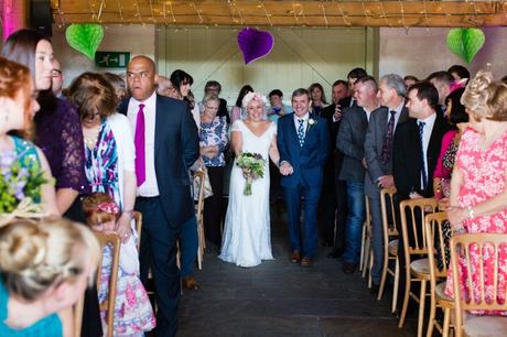 Alternative bride with pink hair and flower crown walks up aisle at East Riddlesden Hall wedding. 