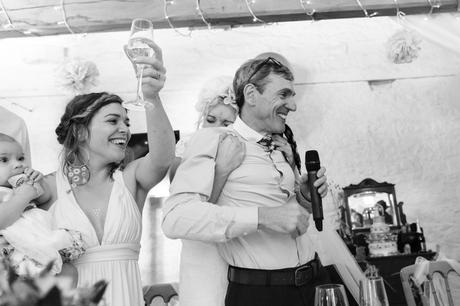 Bride gives dad big hug whilst sister toasts with wine glass at fun and emotional wedding in Yorkshire. 